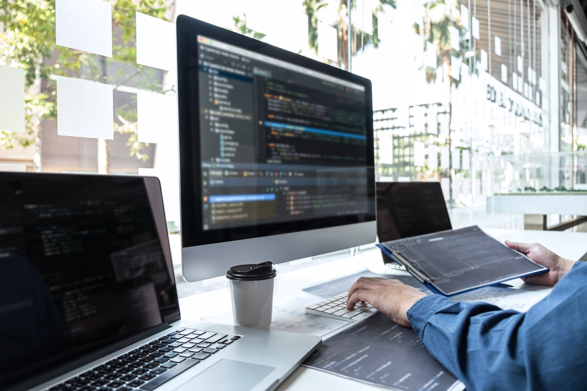 Web家のロゴが入ったマグカップと、コードを表示したノートパソコンが置かれたデスク
