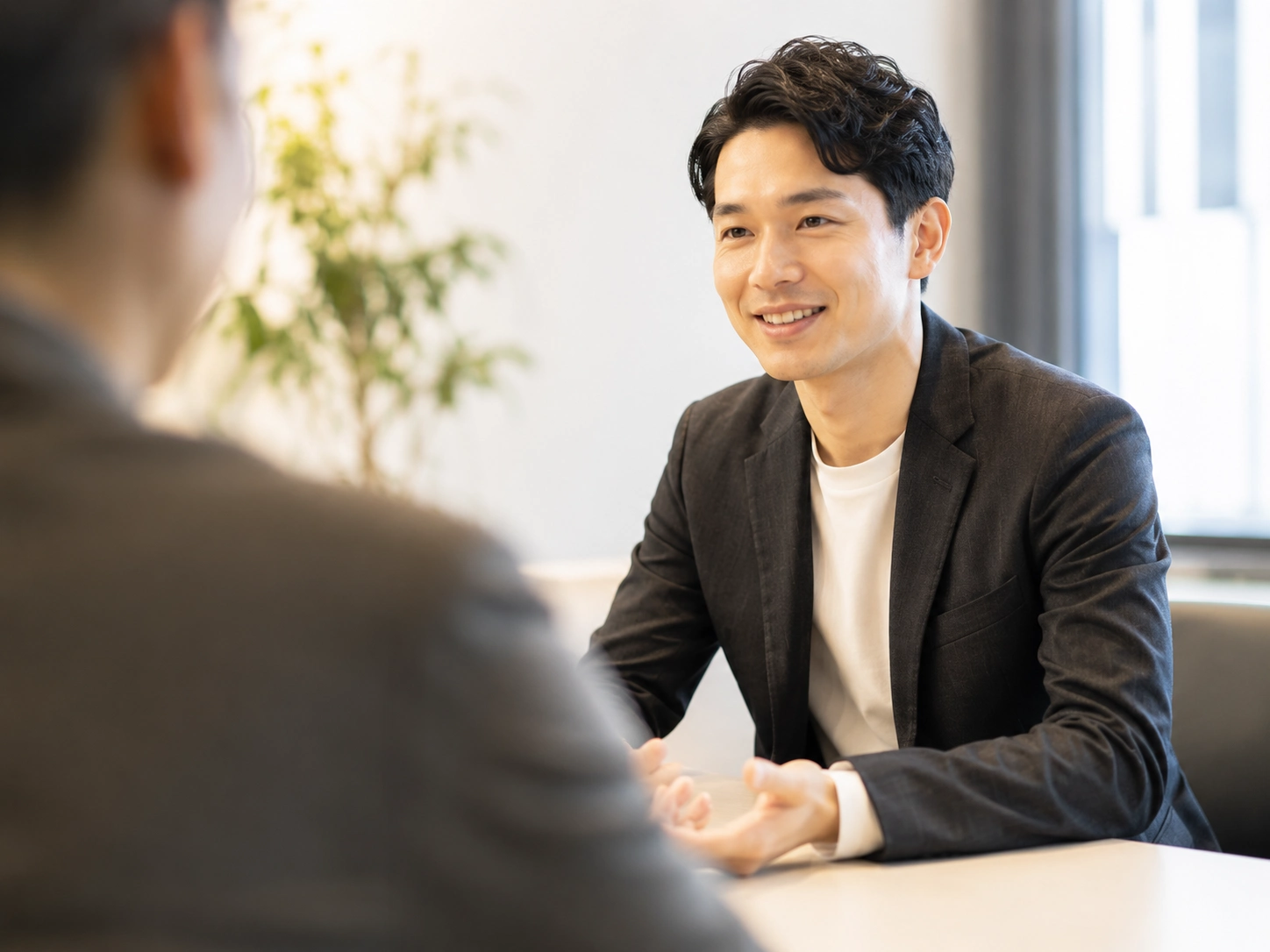 オフィスで笑顔で相談を受ける、ジャケットを羽織った日本人男性