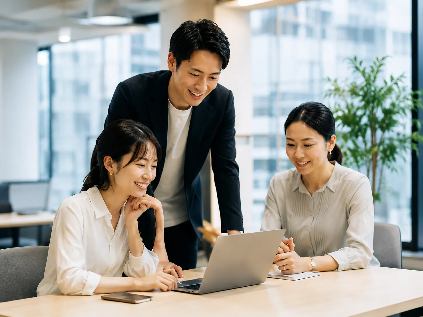 オフィスでノートパソコンを囲んで打ち合わせをする3人の日本人ビジネスパーソン